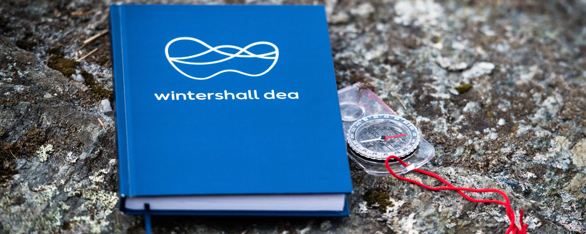 Wintershall Dea Notizbuch und Kompass liegen auf steinigem Untergrund
